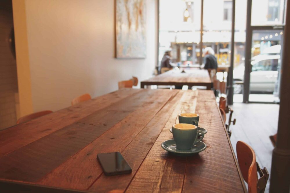 A cafe with a phone phone and cups of coffee on an empty table